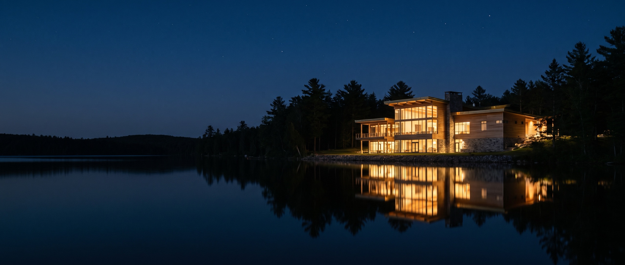 A modern lakeside facility at blue hour, warm windows mirrored in still water